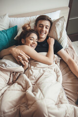Upper view photo of a caucasian couple lying in bed covered with a blanket smiling and embracing