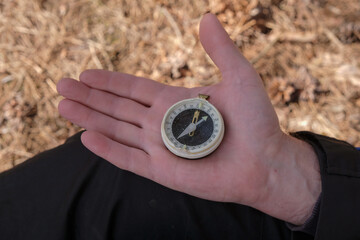 Old compass on a man's palm during hiking. Dry leaves as a blurred background.