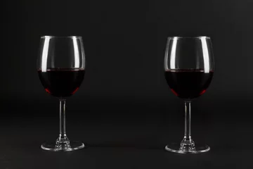 Fotobehang Two glass glasses of red wine on a black homogeneous background © ones88