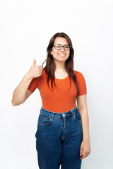 A photo of a young girl looking and smiling at the camera holding a thumb up near a white wall