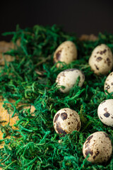 Top view of quail eggs on green grass and rustic wooden table, black background, vertical, with copy space