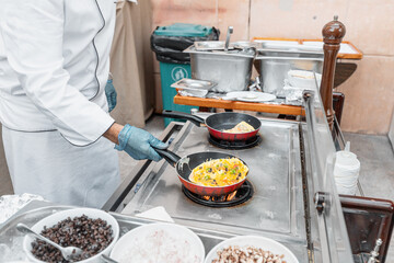 Gloved chef prepares an omelet stuffed with mushrooms and vegetables on a gas stove