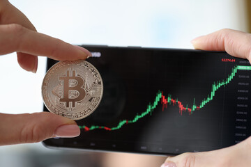 Holding Bitcoin and smartphone with cryptocurrency growth charts