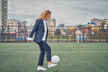 girl in an office suit hitting hitting soccer ball on the stadium field. concept