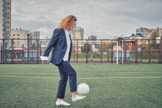 girl in an office suit hitting hitting soccer ball on the stadium field. concept - Powered by Adobe