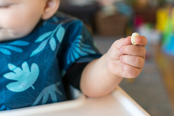 Baby holding a cereal puff in their hand using pincer grasp: developmental milestone self feeding