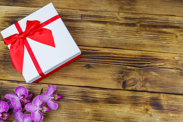 Gift box and orchid flower on a wooden background. Top view, copy space