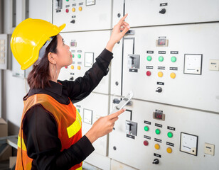 Young Asian female electrical engineers consult and inspect the operation of the electrical control cabinet in an industrial factory.