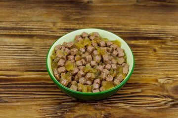 Canned food for cats or dogs in green ceramic bowl on wooden floor