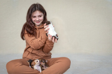 A teenage girl is sitting on the floor, holding a small puppy, with more puppies crawling on her lap, the girl is happy.