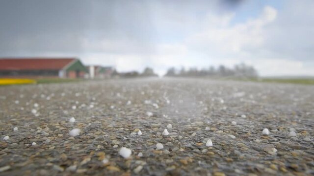 Hail falling on a country road in a rural landscape during a springtime storm. Slow motion clip.
