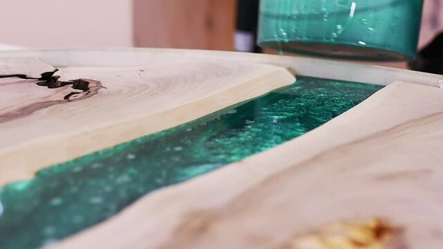 Process making of a craft resin and wood table. Liquid epoxy is poured into a mold with wooden blanks.	