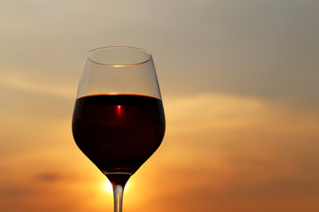 Glass with red wine on sunset background, evening sun is shining through the glass. Concept of celebration, wine industry