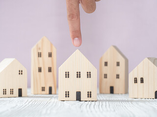 Hand choosing wooden house model from row of model on white wood table, selective focus. Planning to buy property. Choose what's the best. Mortgage and real estate property investment.