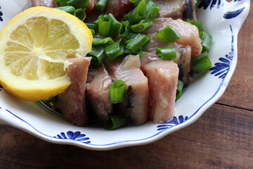 Sliced salted herring fish on a plate with chopped green onion and lemon slice. Swedish pickled herring on wooden table background. Midsummer traditional food. Top view, copy space
