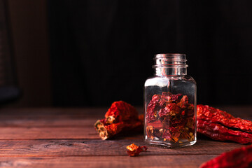 whole pieces of dried pepper lie on a wooden table, and cut pieces of it in a glass jar next to it