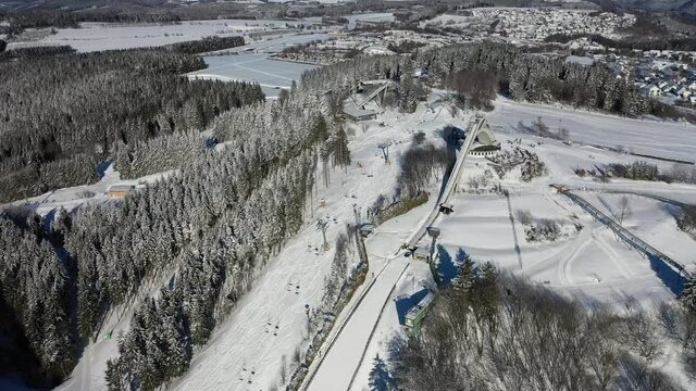 St. George ski jump and ski slopes from ski lift Karussell Winterberg filmed from the air. In the sunshine some people are tobogganing. Flight towards the ski jump.