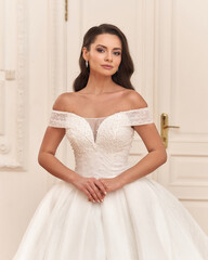 Elegant caucasian woman in white bridal dress standing and posing in bright interior