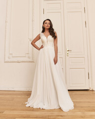 Young pretty caucasian woman standing in bright empty interior and posing in elegant wedding dress