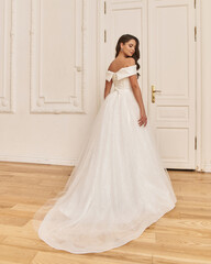 Fototapeta premium Young beauiful happy bride wearing white wedding dress and posing in bright empty interior