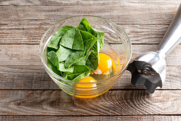 Eggs and spinach in a glass bowl, raw ingredients for cooking healthy spinach pancakes on table. Gluten free spinach pancakes recipe