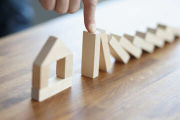 Male hand stoping falling wooden blocks on toy house closeup