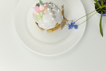 Orthodox Easter cake with white fondant and marshmallows tied with a rope on a plate with spring flowers in a pot top view
