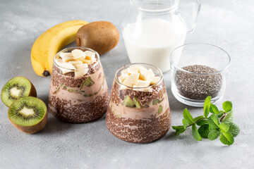 Ingredients for making chocolate chia pudding with banana and kiwi on gray table.