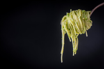 Spaghetti with green pesto sauce made with wild garlic rolled on a fork. Isolated over black...