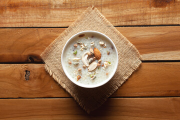 Close-up of Creamy Sabudana Kheer Garnished with dry fruits. Indian delicious dessert. Served in the white ceramic bowl. Top View on wooden background and jute mat.