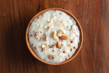 Close-up of Creamy Sabudana Kheer Garnished with dry fruits. Indian delicious dessert. Served in an earthen pot. Top View on wooden background.
