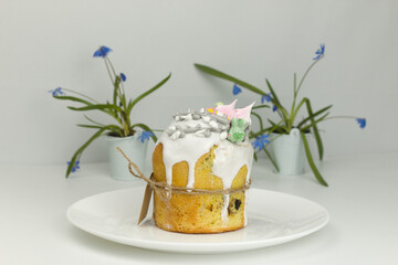 Orthodox Easter cake with white fondant and marshmallows tied with a rope on a plate with spring flowers in a pot, side view