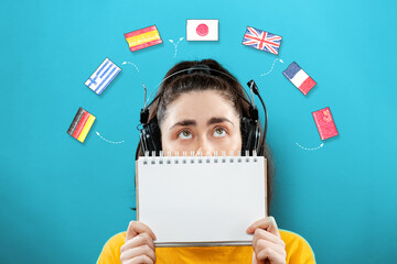 Portrait of a young woman wearing headphones, holding a notebook and looking up at the flags of...