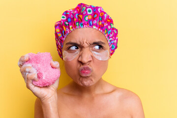 Young mixed race woman taking a bath holding a sponge with an under eye patches