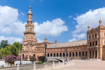 Obraz premium Spanish Square, in the center of Seville. Very touristic travel destination empty due to coronavirus measures. View of the south tower. Coloured flowers, blue sky with few clouds. 