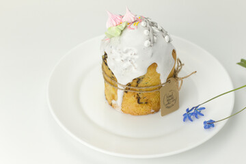 Orthodox Easter cake tied with a rope with a tag on a plate with spring flowers in a pot side view on a white background