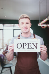 Store owner man holding open sign broad at entrance door of restaurant and coffee shop for telling customers that shop is ready to service.