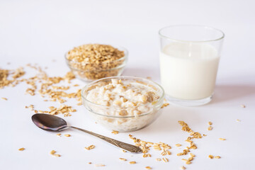 Oatmeal in a plate with a glass of milk and a spoon on a white background.