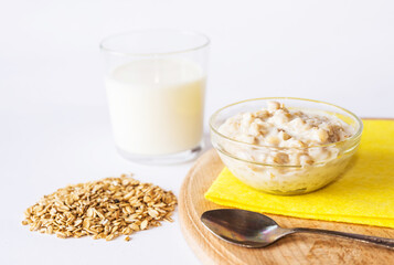 Oatmeal in a plate with a glass of milk and a spoon on a wooden board.