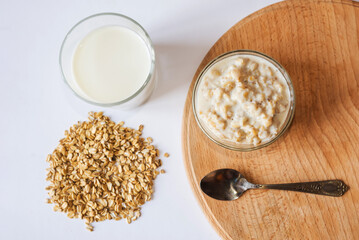 Oatmeal in a bowl with a glass of milk, a spoon and oatmeal on a wooden board. A healthy and nutritious morning breakfast.