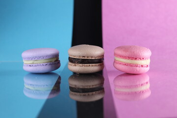 Three macaroons on a blue black pink background different colors different tastes with place for text and reflection