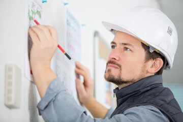man wearing safety-helmet writing information on noticeboard