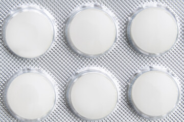 Six white pills in blister on white background