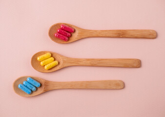 Top view flat lay wooden spoons red,yellow and blue pills on a beige background