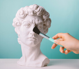 Plaster statue head blue background and female hand  with make up brush