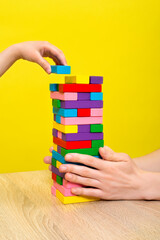 Hands close up playing a round of family game removing blocks from the tower with wooden blocks....