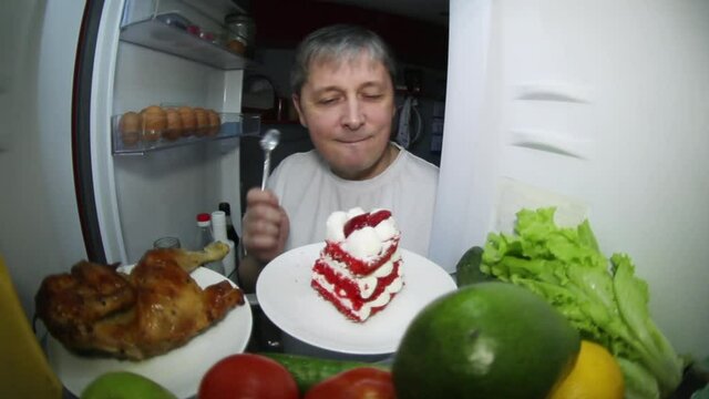 A man looks for food in the refrigerator. Makes a choice: smoked chicken or a piece of cake