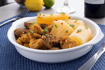 Meat with manioc on a white plate with lemon, glass and wine in the background