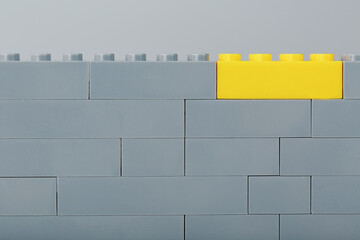 A gray wall made of a toy construction set with the last yellow brick
