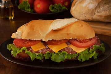 A tomato, cheese, salami and lettuce sandwich, with unfocused tomatoes in the background.